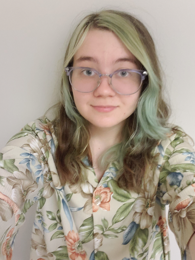 a young man with glasses and long, blonde hair smiles at the camera