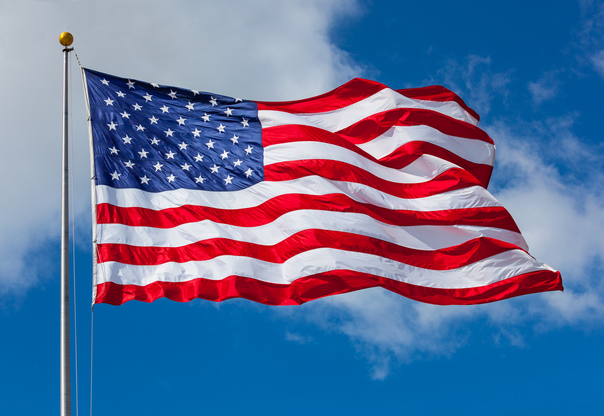 photo of the United States flag flapping on a flag pole against a blue sky
