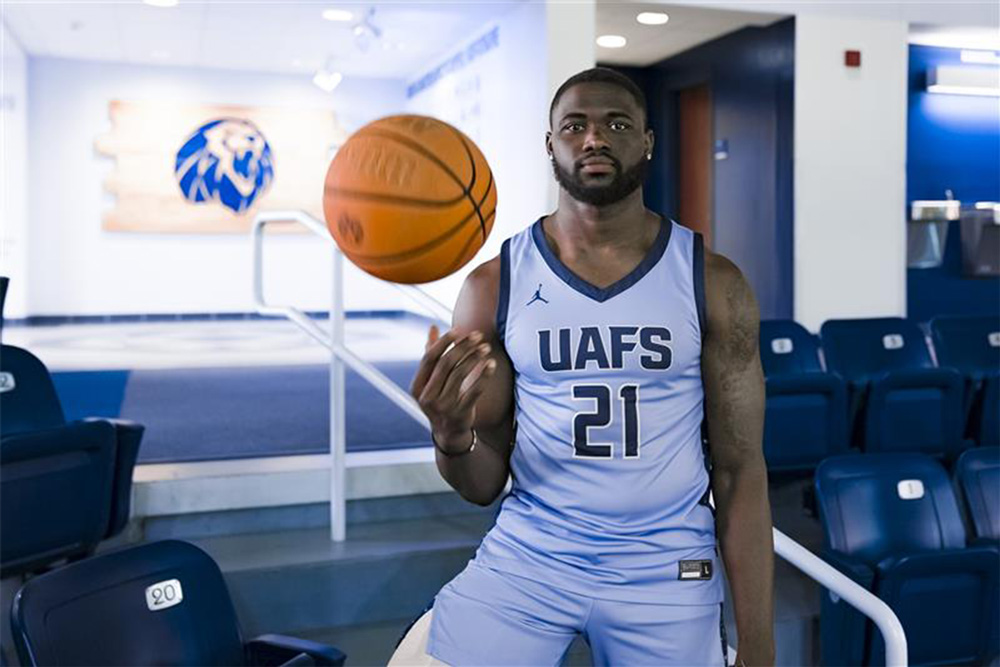 Jarren McAllister stands in the Stubblefield Arena seats tossing a basketball in one hand