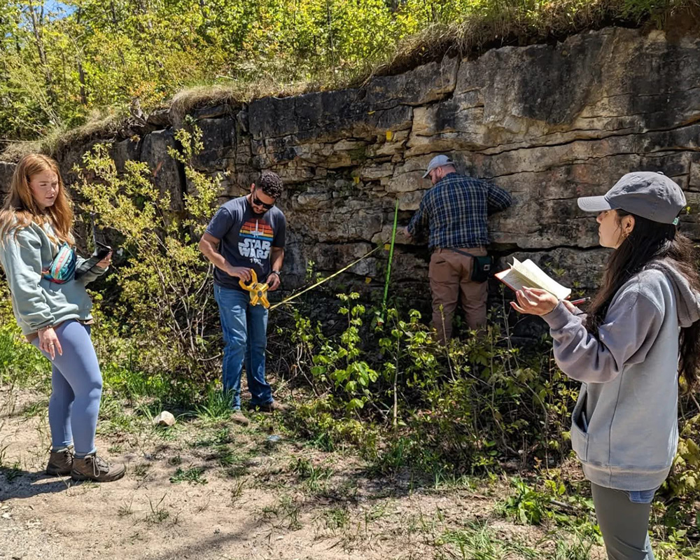 Kaleb McLaughlin, center, takes measurements while conducting research in the field