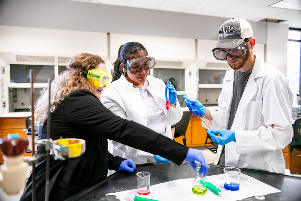 Associate Professor of Chemistry, Dr. Jordan Mader, works with students in a chemistry lab as they mix and measure liquid compounds