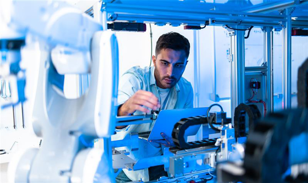 A man programs a piece of robotic equipment in an advanced manufacturing engineering lab