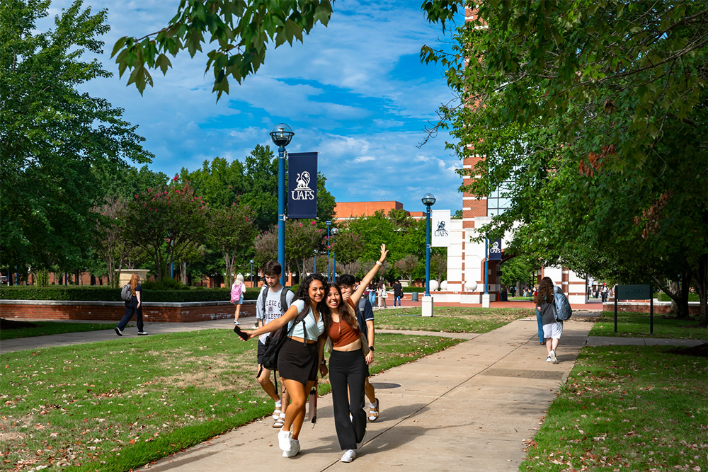 Two students pose on the sidewalk near the UAFS Bell Tower while others walk to class during the first day of the fall semester